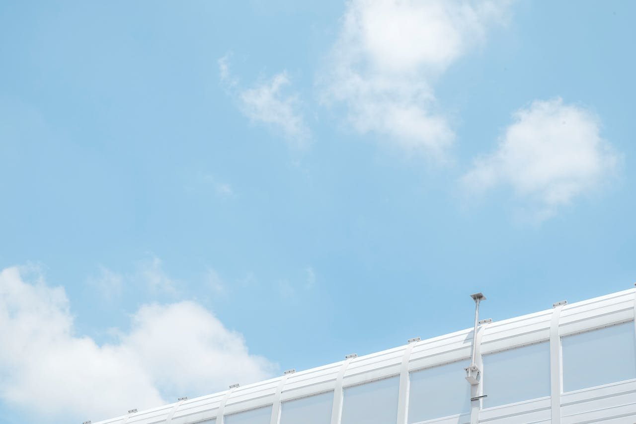 Minimalist image of a security camera against a bright blue sky with scattered clouds.