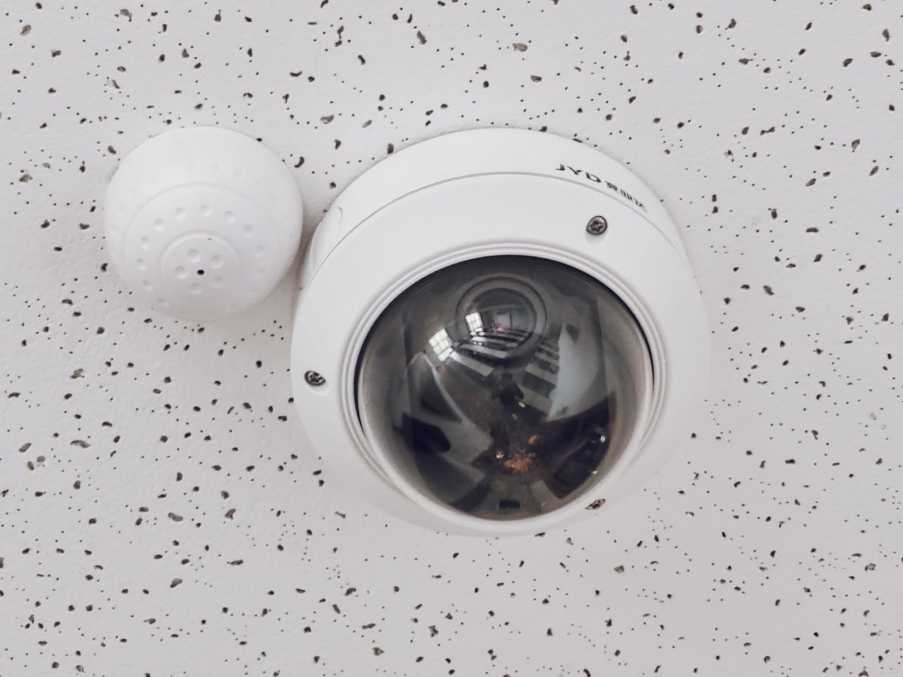 Close-up of a round dome surveillance camera installed on a speckled ceiling for security monitoring.